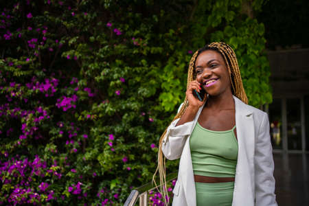 Sportive black woman talking on the mobile while smiling next to a gardenの写真素材