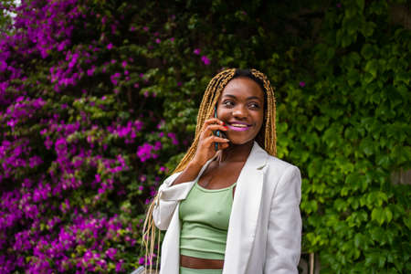 Sportive african woman talking on the mobile while smiling next to a gardenの写真素材