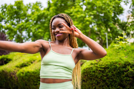 Sportive african woman taking a selfie while gesturing victory outdoorsの写真素材