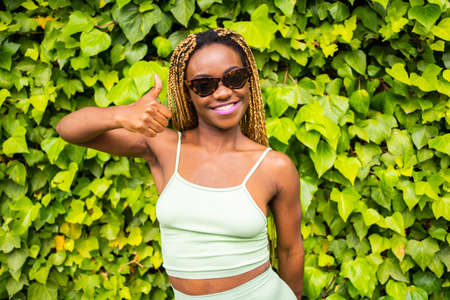 African woman with sunglasses gesturing to be okay facing the camera outdoorsの写真素材