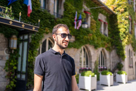 Man with sunglasses next to a medieval building with climbing plants and flagsの写真素材