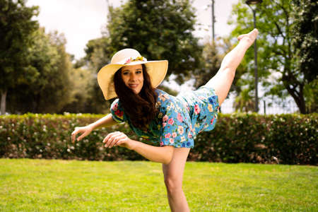 Woman in dress and hat raising the leg while dancing on the grass of a gardenの写真素材