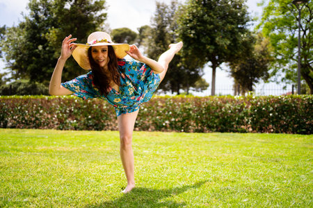 Woman in dress and hat raising the leg while holding the hat and dancingの写真素材