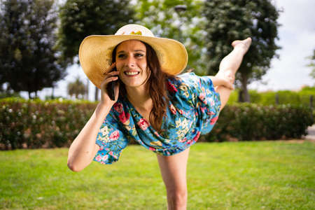 Woman talking to the mobile while raising the leg to dance outdoorsの写真素材