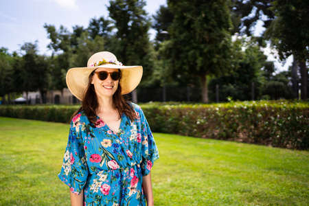 Portrait of a woman in sunglasses and straw hat standing on a garden under the sunの写真素材