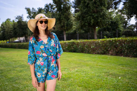 Woman in sunglasses and straw hat standing on a garden under the sunの写真素材