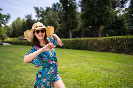 Woman in sunglasses and straw hat dancing and smiling outdoorsの写真素材
