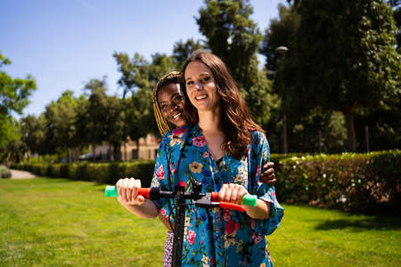 Two multiehnic women on an electric scooter outdoorsの写真素材