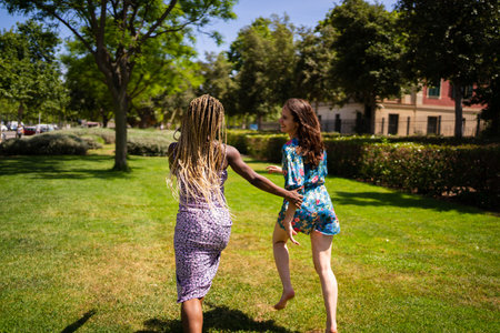 Back of two women of different ethnicities running holding hands in a gardenの写真素材