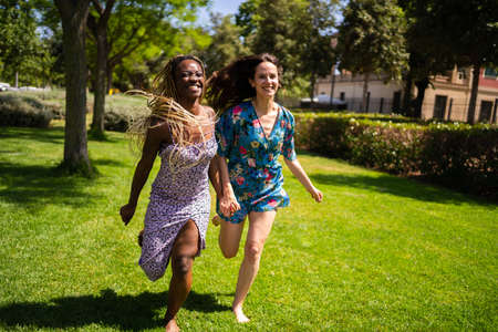 Two multiethnic women running holding hands outdoorsの写真素材
