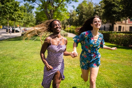 Two happy multiethnic women running holding hands outdoorsの写真素材