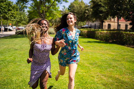 Two multiethnic women smiling while running holding hands outdoorsの写真素材