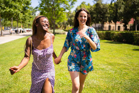 Two multiethnic women having fun while running holding hands outdoorsの写真素材