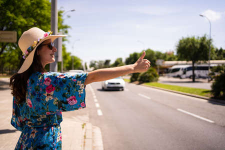 Profile of a woman in floral summer dress and hat hitchhiking next to a streetの写真素材