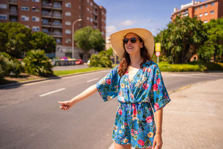 Portrait of a woman in floral summer dress and hat hitchhiking next to a streetの写真素材