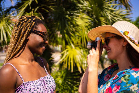 Woman in straw hat taking pictures with a camera of a black womanの写真素材