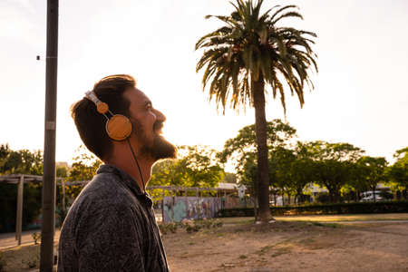 Caucasian man with a beard listening to music with headphones outdoorsの写真素材