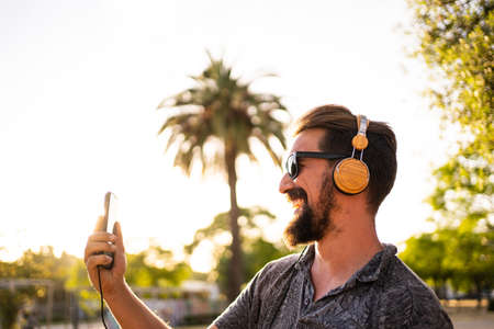 Man with a beard listening to music with a mobile phone in the street at sunsetの写真素材
