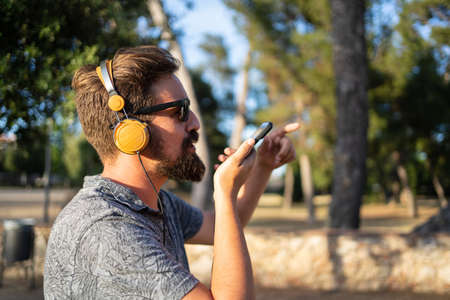 Profile of a man sending a voice message with his mobile phone outdoorsの写真素材