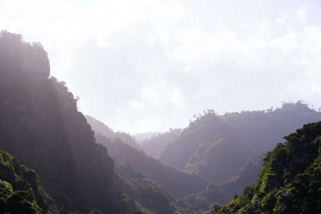 Sun illuminating a mountain range with wild green plants in a cloudy dayの写真素材