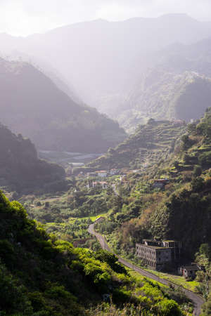 Road in the middle of a mountain range with tropical vegetation and some buildings.の写真素材