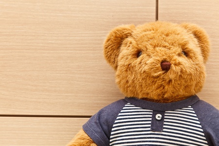 A fluffy brown bear doll in blue and white t-shirt with wooden backgroundの写真素材
