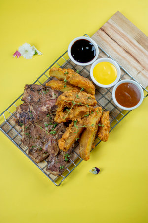 Grilled lamb steak with potato wedges and sauces on a yellow background. Good for any festive or family gathering.の写真素材