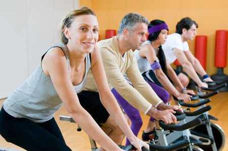Happy people in a row exercising with bicycles in a gymの写真素材