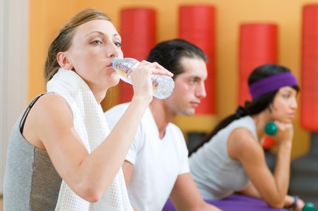 Beautiful young lady drinking bottle of water during a break at gymの写真素材