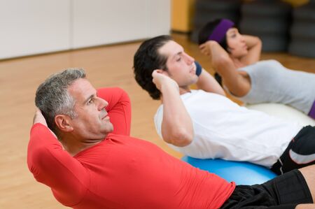 Healthy people with mature instructor doing sit-ups on fitness ball at gymの写真素材