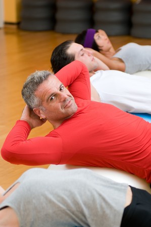 Healthy people with mature instructor doing sit-ups on fitness ball at gymの写真素材