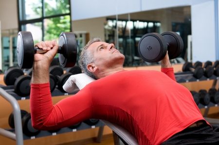 Mature man lifting dumbells at fitness gymの写真素材