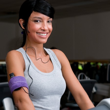 Portrait of beautiful young latin woman smiling and listening music while walking on a treadmill at gymの写真素材