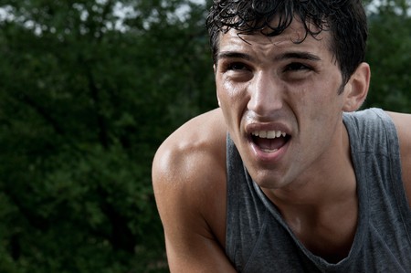 Young exhausted latin man looking at the rest of path during a break of his outdoor jogging trainingの写真素材
