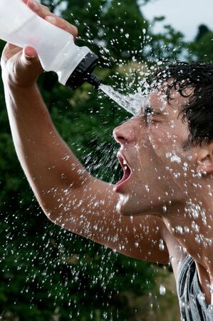 Young tired athlete splashing and pouring fresh water on his head to refresh during a running trailの写真素材