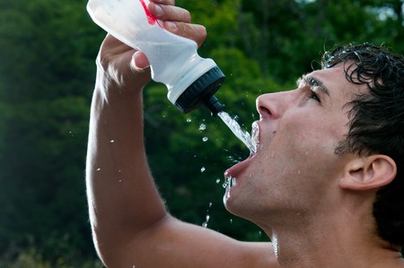 Young exhausted athlete drinking and pouring fresh water to refresh during a running trailの写真素材