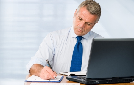 Absorbed mature businessman working and taking notes in his modern officeの写真素材