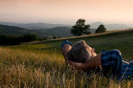 Closeup view of mature man taking a break and relax in a meadow in the wonderful warm light of the sunsetの写真素材