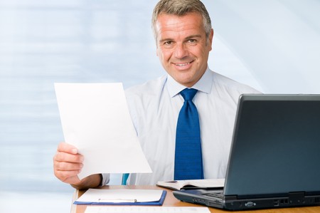 Mature positive businessman holding paperwork and looking at camera smilingの写真素材