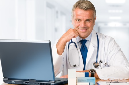 Happy satisfied mature doctor working and looking at camera in his modern clinic officeの写真素材