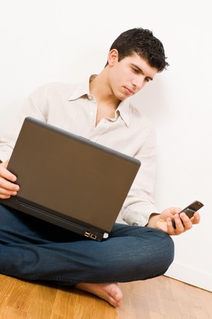 Young man in casual clothing working on his laptop and looking at mobile phoneの写真素材