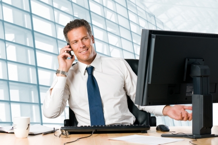 Successful businessman sit at his desk while talking on mobile in officeの写真素材