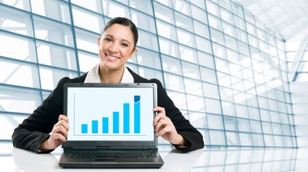 Young business woman displaying successful growing graph on her laptop in a modern officeの写真素材