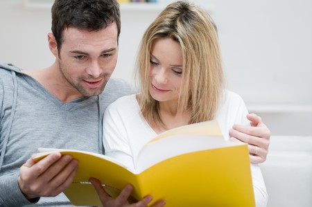 Young couple reading together a magazine in their living room at homeの写真素材