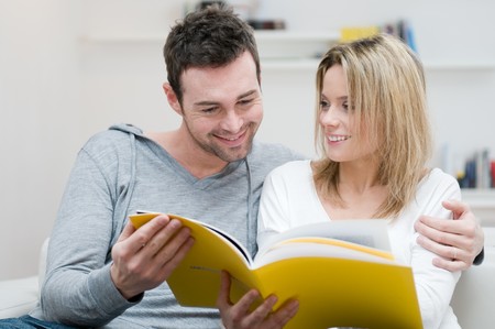 Young couple reading together a magazine in their living room at homeの写真素材