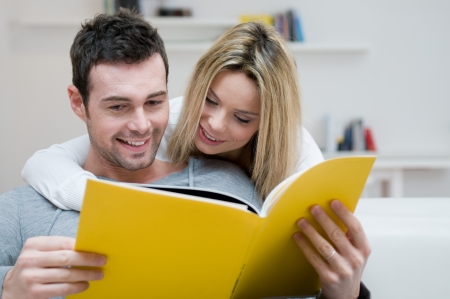 Young couple reading together a magazine in their living room at homeの写真素材