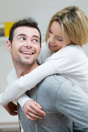 Young couple piggybacking and have fun at home with knowing glanceの写真素材