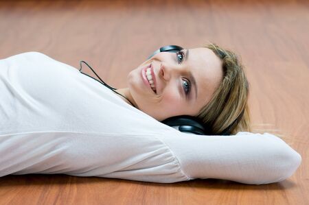 Young girl listening relaxing music with headphones lying on wooden floorの写真素材