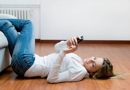 Young beautiful woman text messaging on mobile while relaxing on the floorの写真素材