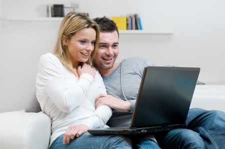 Young couple relaxing on the couch with laptop in their living room at homeの写真素材